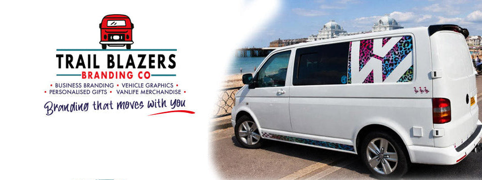 A white van with a large colorful 'W' logo decal on the side window, parked outdoors beside a waterfront. The left side of the image features a logo for Trail Blazers Branding Co with text about branding and vehicle graphics.